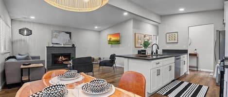 This open-concept space features a cozy living area with a fireplace, a stylish kitchen with an island, and a warm dining setup. Modern lighting, wood floors, and elegant decor create a welcoming atmosphere.