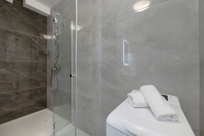A clean, modern bathroom with grey tiles, a glass-enclosed shower, and a minimalist white sink. It has a sleek, modern look.