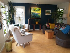 Main house living room is cozy with original art, big windows, lots of plants.