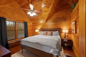 Cozy bedroom with king bed, wood walls, vaulted ceiling, and serene window views