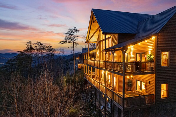 A welcoming porch beckons guests into this cozy twilight cabin retreat, where warm lights and rustic charm invite you to unwind and relax. 🏡✨