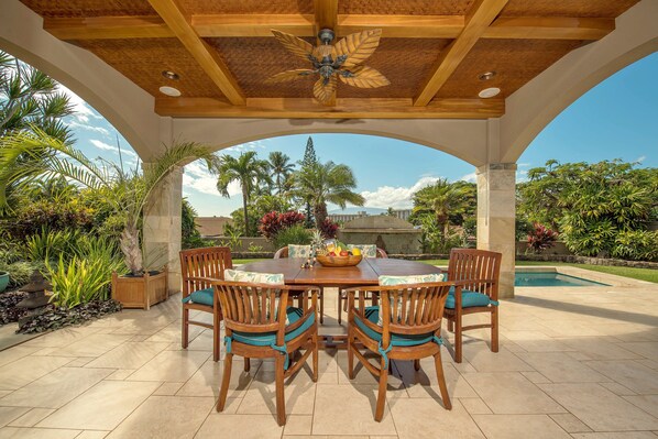 Relax in the covered lanai, complete with ceiling fans and a view of the pool and tropical landscaping, ideal for unwinding after beach adventures.