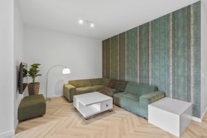 Living area featuring green modular seating, an accent wallpaper, and a white coffee table on a soft rug.