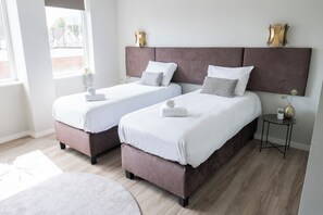 This bright and cozy bedroom features two single beds with soft headboards, dressed in crisp white linens. Golden wall sconces and minimalist bedside tables add elegance and functionality. Bed and Coffee in Raamsdonksveer is your affordable hotel alternative, just steps from the centre.