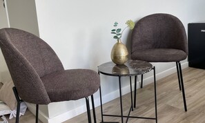 This intimate seating area is furnished with two upholstered chairs and a black round table. The golden vase centerpiece and soft textures add a touch of elegance, making it a perfect spot for relaxation or conversation.