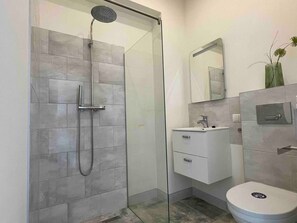 The bathroom showcases a stylish and functional design with a walk-in shower enclosed by a glass partition, a compact vanity with a sink, and a wall-mounted toilet. Neutral tiles and subtle decor create a clean and contemporary ambiance.