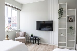 Light-filled bedroom corner with a cozy seating area, smart TV, and stylish shelving — perfect for relaxation and entertainment.