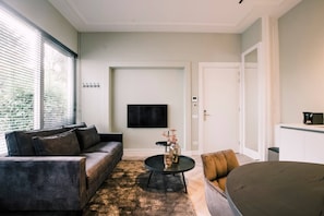 A stylish and comfortable living room with a plush sofa, perfect for relaxing while enjoying the natural light streaming through the large windows. The space is complemented by a modern TV and cozy decor, offering a calm and inviting atmosphere.