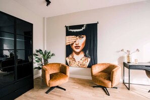 A stylish room with two cozy caramel armchairs, bold wall art, a sleek black desk, and modern decor, complemented by a black glass wardrobe and greenery.