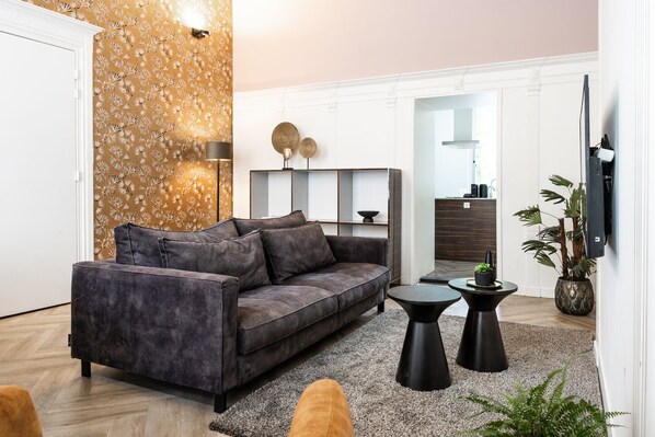 Stylish living space with a dark velvet sofa, black coffee tables, warm gold accent wall, and modern decor—blending comfort and contemporary elegance.