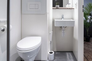 A minimalist bathroom featuring a toilet, a modern sink, and efficient storage, creating a functional and stylish space in a small area.