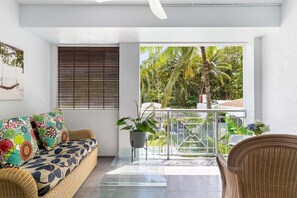 Unwind overlooking the luscious shared gardens from the furnished balcony. There are two wicker chairs, a table and a lounge shaded comfortably undercover. 
