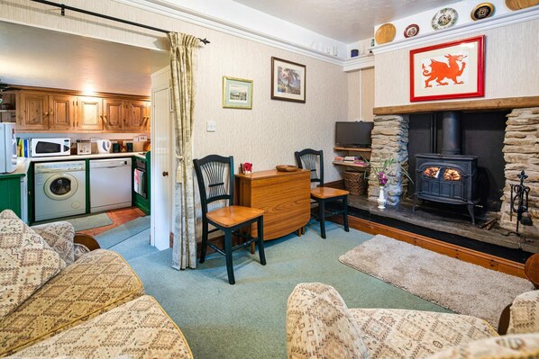 Lounge and dining area with sofa, woodburner, fold down table with two dining chairs.