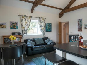Open plan living area with sofa, table and chairs, kitchen with breakfast bar