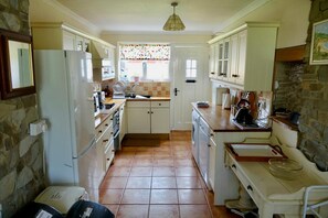 Glanyrafon Smithy kitchen with units, fridge freezer, tiled floor and doorway