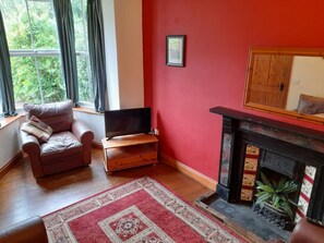 Fireplace with wooden mantlepiece, mirror above, small flat svreen tv on unit and leather armchair