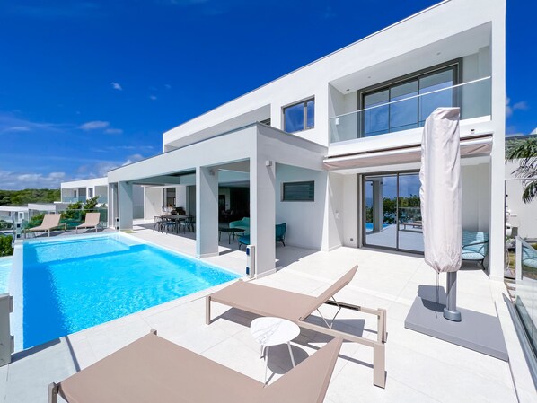 Overflowing pool, deckchairs and parasol on a shaded terrace facing the sea