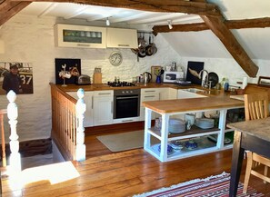 Open kitchen with extended worktop with open storage underneath, oven and cooker top.