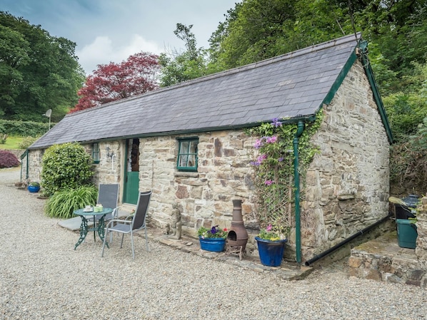 Cottage with gravel patio area with small table and chairs, surrounding trees