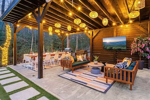 Indulge in nature within the luxurious setting of a spacious pergola equipped for grilling, dining, relaxing with a TV, and unwinding in a lounge area.