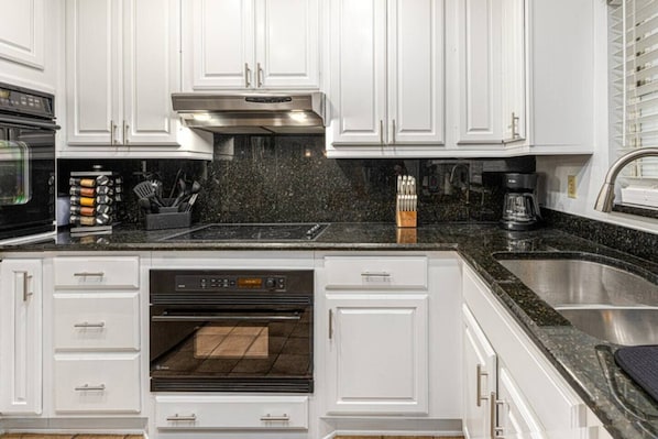 Kitchen with oven, sink, microwave, storage cabinets, knife set, spice rack, coffee maker, utensils.