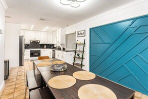 Bright and spacious kitchen with a modern dining area, featuring a bold blue accent wall, tiled floors, and sleek white cabinetry for a stylish and welcoming atmosphere.