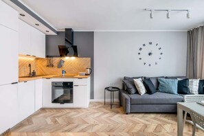 A view of the kitchen and living room with herringbone flooring and a mix of white and wood finishes.