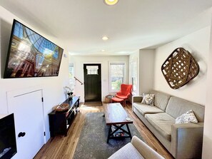 Living room with Smart TV, electric fireplace, games, magazines, and reading chair.