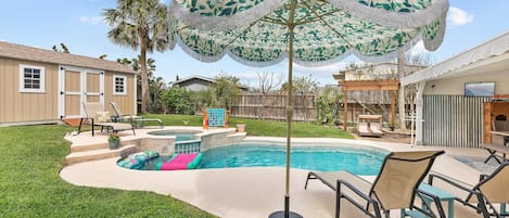 Relax in this serene backyard oasis featuring a pool, hot tub, and lush tropical landscaping. Enjoy the shade under a stylish umbrella and lounge on comfortable chairs for ultimate outdoor living. Perfect for your next getaway!