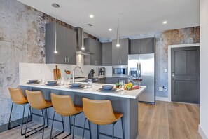 Unit 1: Fully equipped kitchen with stainless steel appliances, basic cooking essentials, coffee machine, and kitchen island seating.