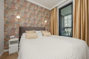 A cozy bedroom with patterned wallpaper, a soft bed, and warm lighting, blending elegance with comfort.

