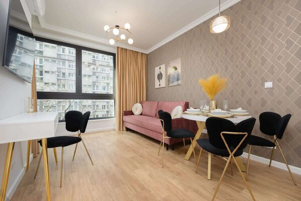 A stylish living and dining area featuring a modern chandelier, a pink velvet sofa, and gold-accented decor creating a luxurious ambiance.

