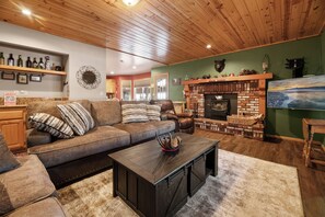 Living Room with Fire Place - Warm wood ceilings glow in the living room, furnished with a plush sectional and armchair. Settle in and watch a film on the 50-in smart TV while the wood-burning fireplace crackles. Features a DVD collection and board game selection!