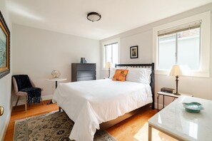 Third bedroom with natural light, double size bed with premium mattress and bedding, dresser, laptop workspace with marble bistro table and geometric lamp.