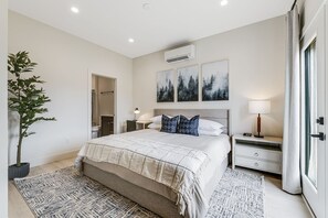 Master bedroom with attached master bathroom, king bed, walk-out patio deck, work desk with chair & lamp, large walk-in closet, night stand, and clothes dresser
