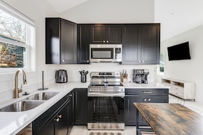 Interior-designed and fully-stocked modern kitchen with stainless steel appliances, granite countertops, and a cute kitchen island with 2 small bar stools