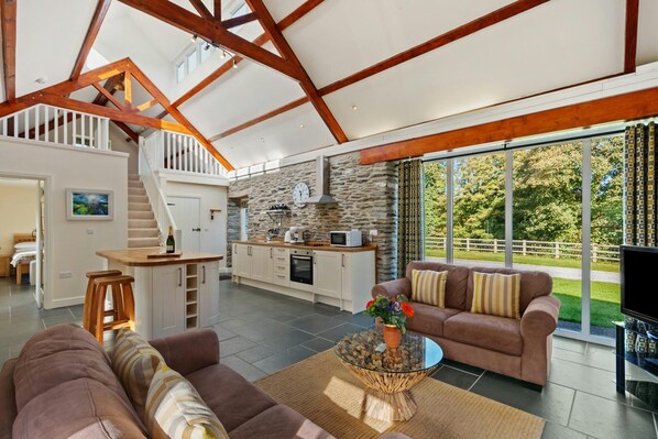 Sofas, coffee table with flowers in the living area looking towards the kitchen area