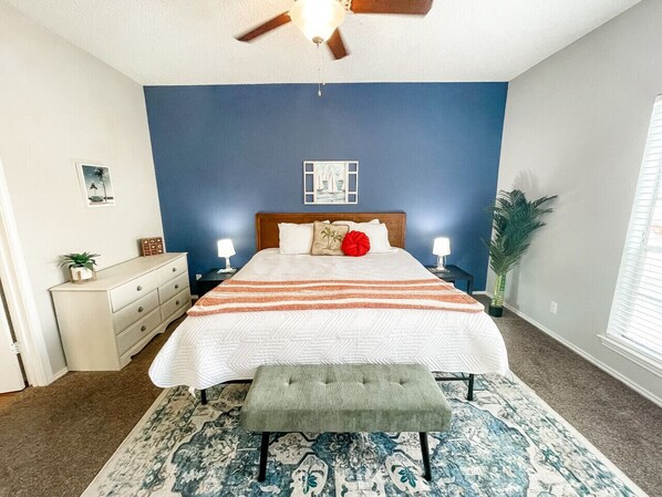 Bright master bedroom with natural light, linens, fan, decor, and storage.