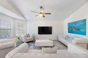 Luxurious modern white living room in Navarre, FL with 75" HDTV & local art.