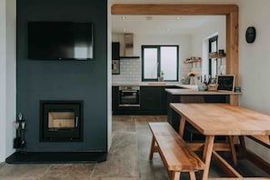 Ty Melyn No.2 Newgale – A warm, welcoming open-plan space with wood-burning stove and handcrafted dining table for sharing meals and stories.
