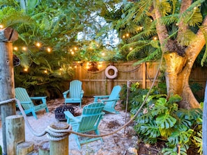 Fairy-lit tropical nook: turquoise chairs circle a fire pit, perfect for sunset sips and starry chats.