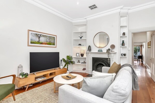 The living room exudes a serene and cosy ambience, thanks to the inviting reading chair, floor lamp, and the original heritage decorative fireplace.