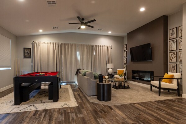 Open concept living area with pool table, fire place, comfortable seating and classy decor.
