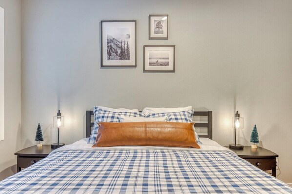 Cozy up in this inviting bedroom with mountain-chic plaid bedding, warm leather accents, and soft lighting—your perfect retreat after a day of adventure.