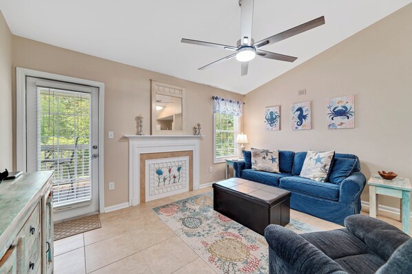 The spacious living room exudes coastal charm with its classic nautical decor and furniture. The modern ceiling fan offers additional temperature control for your convenience.