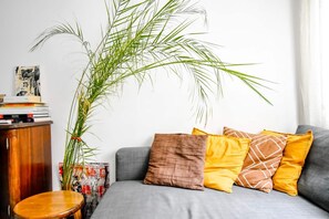 A cozy living room corner with a comfortable gray sectional sofa adorned with vibrant yellow and brown pillows, set against a backdrop of white walls and a tall green plant, inviting relaxation and socializing.