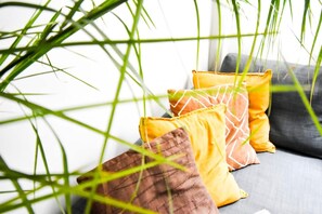A cozy living room corner with a comfortable gray sectional sofa adorned with vibrant yellow and brown pillows, set against a backdrop of white walls and a tall green plant, inviting relaxation and socializing.