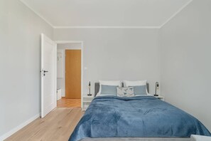 A cozy bedroom featuring a bed with a blue bedspread and wooden flooring.