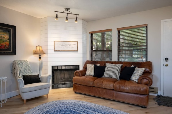 Experience the cozy living room, outfitted with plush seating, a fireplace, an expansive smart TV, and windows that frame views of the great outdoors.