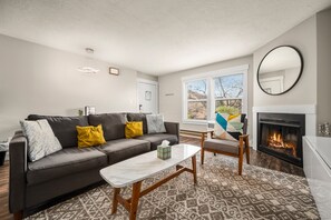 Experience the cozy living room, outfitted with plush seating, a fireplace, an expansive smart TV, and windows that frame the views of the great outdoors.